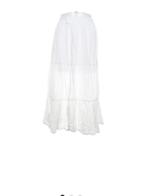 Vit långkjol i viscosa med volang - Luftig vit långkjol i bomull med bred resår i midjan och volangdetaljer. Kjolen har en avslappnad passform och är perfekt för varma dagar. Enkel och stilren design som passar till många olika looks.