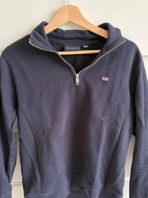 Marinblå halfzip från Lexington - Snygg marinblå sweatshirt från Lexington med halv dragkedja och liten flagglogga på bröstet. Tröjan har ribbade muddar och är tillverkad i mjuk bomull. Perfekt till jeans för en clean och avslappnad stil.