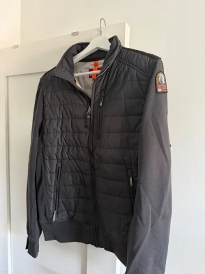 Mörkgrå Parajumpers jacka fleece M - Snygg mörkgrå jacka från Parajumpers med quiltad front och släta ärmar. Jackan har dragkedja, två fickor fram och en patch på axeln. Insidan är fodrad med fleece för extra värme. Perfekt för kyliga dagar och enkel att matcha.