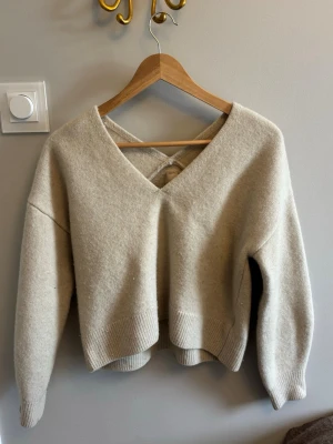 Beige stickad tröja med v-ringning - Säljer en beige stickad tröja med djup v-ringning och snygg detalj i ryggen.  Tröjan är kort. 