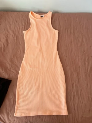 Ljus ribbad ärmlös klänning - Säljer en ljus, ribbad klänning i figurnära modell. Klänningen är ärmlös med hög hals och har en enkel, stilren design som passar perfekt till sommaren. Materialet känns mjukt och stretchigt, vilket gör den bekväm att bära.