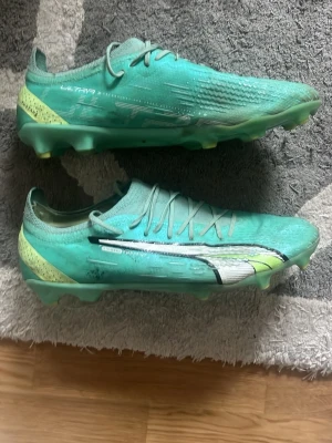 Puma Ultra gröna fotbollsskor ultimate Elite - Säljer ett par snabba Puma Ultra fotbollsskor i mintgrönt med gula och vita detaljer. Skorna har låg profil, klassisk snörning och en lätt ovandel i syntetmaterial för maxad fart på planen. Perfekta för dig som vill sticka ut och dominera matchen. Elite, Ultimate. Ny pris ca 2500kr