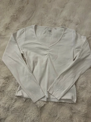 Vit långärmad topp med v-ringning - Säljer en enkel och stilren vit långärmad topp från Lager 157. Toppen har en snygg v-ringning med rynkdetalj framtill och är gjord i mjuk bomull. Perfekt att matcha med jeans eller kjol för en clean look. Säljer den då den är för stor för mig. Bär vanligtvis S eller XS så den lite större för sin storlek. Aldrig använd