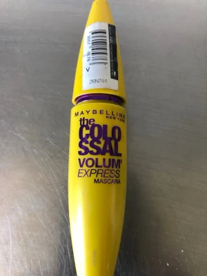 Maybelline Colossal Volum' Express Mascara - Gul mascara från Maybelline med lila text, Colossal Volum' Express. Tuben har en avlång, rundad form och är tillverkad i plast. Perfekt för dig som vill ha volym till fransarna och en färgstark förpackning i sminkväskan.