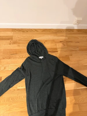 Mörkgrön hoodie från Ahlquist Clothing - Säljer en stilren mörkgrå hoodie från Ahlquist Clothing i storlek S. Hoodien är tillverkad i ett mjukt stickat material som känns skönt mot huden. Perfekt för dig som gillar enkel och clean design.