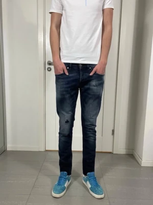 Dondup jeans - Säljer ett par mörkblå slim fit jeans från Dondup med slitningar och tvättade detaljer. Jeansen har klassisk femficksmodell, låg midja och smal passform. Snygga kontrastsömmar och diskret logga bak på linningen.