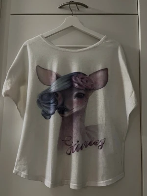 Vit tröja med lila rådjursmotiv - Storlek S/M (34-38) - Kortärmad tröja i vit bas med dekorativt lila rådjursmotiv! Passar dig som vill ha en unik tröja som sticker ut det lilla extra! Storlek: Ingen märkning, uppskattas till S/M (34–38) Säljs i bra skick! Kika gärna in på mina andra annonser, jag säljer just nu flera plagg!