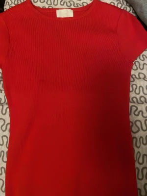 Röd ribbad topp med kort ärm - Snygg röd topp med ribbad struktur tight och korta ärmar. Enkel och stilren design som passar perfekt till jeans eller kjol. Rund halsringning och figurnära passform ger en modern look.