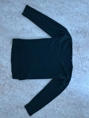 Svart stickad tröja med rund hals - En enkel och stilren svart stickad tröja med rund halsringning och långa ärmar. Tröjan har en smal passform och ribbstickade muddar vid ärmslut och nederkant. Perfekt basplagg för lager på lager och funkar året runt.