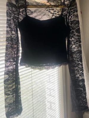 Svart spetsblus med lång ärm - Säljer en svart blus med transparenta spetsärmar och detaljerad spets upptill. Toppen har en croppad passform och vacker spetskant nedtill. Perfekt för dig som gillar en edgy och trendig stil.