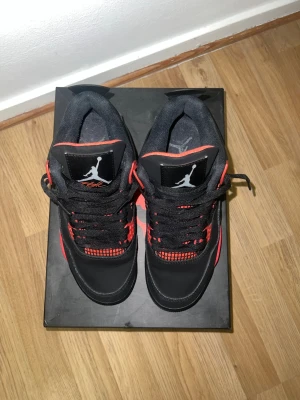 Air Jordan 4 Retro Svart/Röd - Säljer ett par Air Jordan 4 Retro sneakers i svart med röda detaljer. Skorna har klassisk mesh på sidorna, synlig Air-sula och Jumpman-logga på plösen. Materialet är en mix av läder och textil, och färgkombon ger en riktigt clean look.