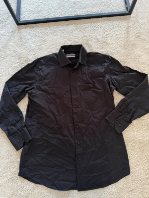 Svart skjorta från Kiğılı Classic - Stilren svart skjorta från Kiğılı Classic med klassisk krage och knappar framtill. Skjortan har lång ärm och är tillverkad i ett mjukt bomullstyg som känns bekvämt mot huden. Perfekt för dig som gillar en enkel men snygg look.