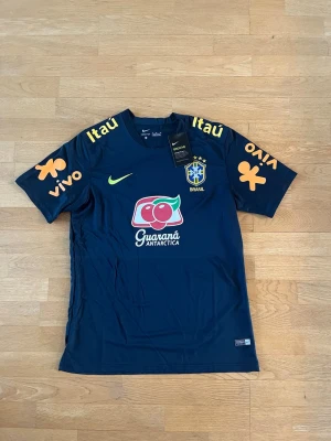 MörkBlå Brasilien träningströja Nike - Mörkblå träningströja från Nike med Brasilien med gula detaljer och sponsortryck från Guaraná Antarctica, Itaú och Vivo.  Perfekt för fotbollsträning eller sportiga aktiviteter.                  Den är lite liten i storlek så passa bra som L också