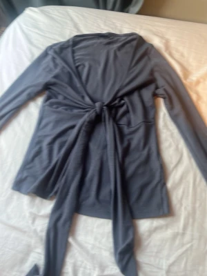 Grå omlottopp med knytband - Snygg grå omlottopp med långa ärmar och breda knytband framtill. Toppen har en djup v-ringning och är perfekt för att skapa en trendig lager-på-lager-look. Materialet känns mjukt och följsamt mot huden.