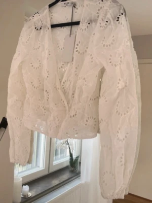 Vit broderad blus från NA-KD - Söt vit blus från NA-KD med broderade hålmönster och v-ringning. Blusen har långa ärmar med lätt puff och resår vid ärmslut. Helt ny och oanvänd med prislapp kvar! 