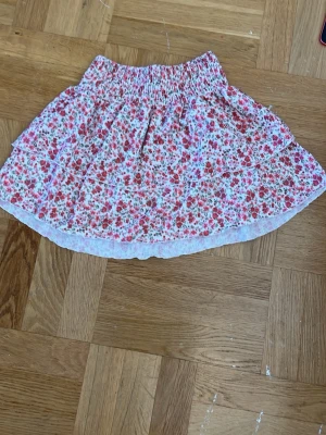 Blommig volangkjol från Gina Tricot - Söt kort kjol från Gina Tricot i storlek XS. Kjolen är vit med små rosa och röda blommor, har volanger och resår i midjan för en bekväm passform. 