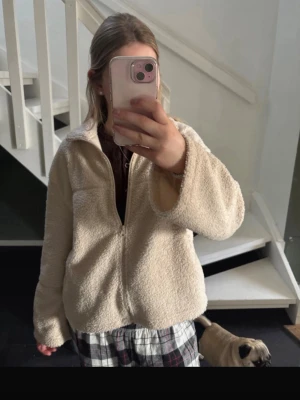 Beige teddyjacka med dragkedja - Mysig beige teddyjacka med dragkedja framtill och hög krage. Jackan har en avslappnad passform och är gjord i fluffigt teddy-material som känns supermjukt. Perfekt för att hålla värmen under kyliga dagar och ger en chill vibe till din outfit. Nästan anvönd 15 gånger ungefär 