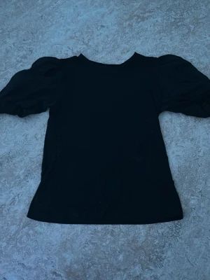 Svart topp med puffärmar - Snygg svart topp med puffiga, korta ärmar och rund halsringning. Toppens material känns mjukt och lätt, perfekt för att lyfta vilken outfit som helst. Enkel men trendig design som passar till mycket.