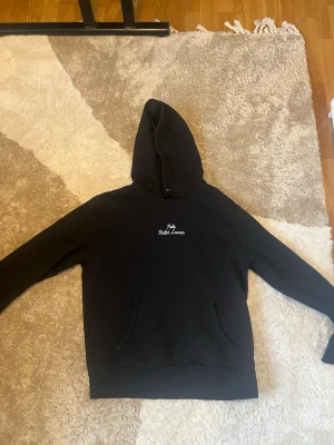 Svart hoodie från Polo Ralph Lauren - Snygg svart hoodie från Polo Ralph Lauren med broderad vit logga på bröstet och liten logga på ärmen. Hoodien är äkta och jag har använt den 1 gång.