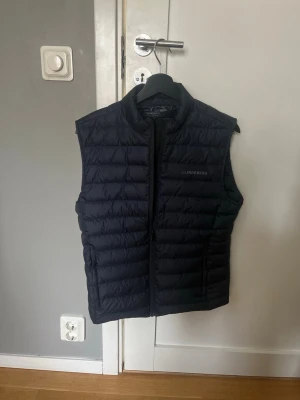  J.Lindeberg väst - Snygg marinblå dunväst från J.Lindeberg med diskret logga på bröstet. Västen har ståkrage, quiltad design och dragkedja framtill. Perfekt nu inför våren / sommaren. Tillverkad i lätt och smidigt material. Storlek: s ( nypris 2190kr kvitto finns )