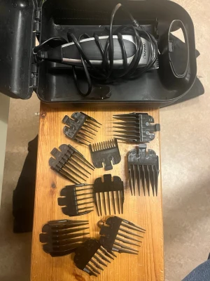 Wahl hårtrimmer med tillbehör - Elektrisk hårtrimmer från Wahl i svart och silver med flera svarta plastkammar i olika längder. Allt ligger i en svart förvaringsväska. Perfekt för att fixa frisyren hemma och anpassa längden med olika kammar.