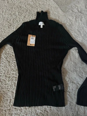 Svart ribbad polotröja från other stories - Säljer en svart, ribbstickad polotröja från Gina Tricot. Tröjan har lång ärm, figurnära passform och hög krage. Materialet är stretchigt och mjukt, perfekt för lager på lager. Enkel och stilren design som passar till det mesta.