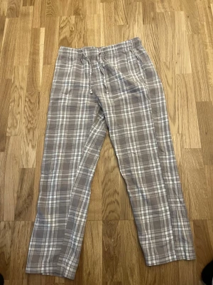 Rutiga pyjamasbyxor från 157 - Mysiga pyjamasbyxor från 157 i beige och vitt rutigt mönster. Byxorna har resår och dragsko i midjan för skön passform. Perfekta för slappa dagar hemma eller när du vill ha det extra bekvämt. Använd få gånger