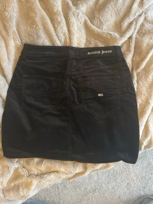 Svart kortkjol från Tommy Hilfiger - Säljer en svart kortkjol från Tommy Hilfiger med klassisk femficksdesign och broderad logga bak i midjan. Kjolen är i mjuk manchester och har en normal passform. Perfekt att sy om till en mini skirt.