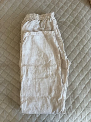 Beige linnebyxor från Chelsea  - Säljer ett par ljusbeige linnebyxor från Chelsea Girls i storlek XS. Byxorna har resår i midjan och är tillverkade i 100% linne, vilket gör dem luftiga och sköna. Perfekta för en avslappnad och trendig look.