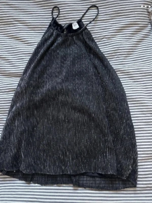 Glittrig mörkblå linnetopp - Snygg glittrig mörkblå linnetopp med tunna axelband och lätt A-linjeform. Toppen har ett subtilt silverglittrande mönster och knapp i nacken. Perfekt för dig som vill sticka ut lite extra.