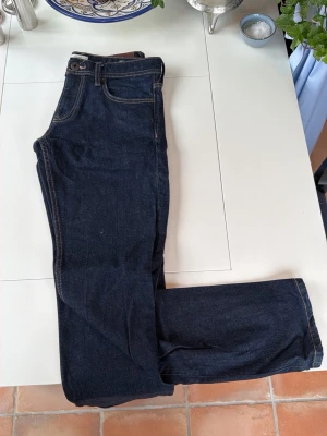 Mörkblå raka jeans - Säljer ett par mörkblå jeans med klassisk rak passform och fem fickor. Jeansen har kontrastsömmar och normal midja. Perfekta till en avslappnad stil och funkar året runt.