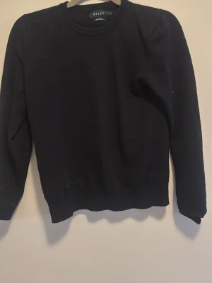 Svart tröja från Riley - En stilren svart tröja från Riley med rund halsringning och långa ärmar. Tröjan har en klassisk passform och ribbade muddar vid ärmslut och nederkant. Perfekt för en enkel och clean look.