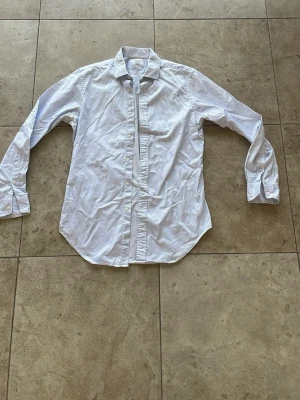 Vit och ljusblå randig skjorta - Klassisk skjorta med tunna ljusblå ränder på vit botten. Skjortan har lång ärm, knappar framtill och en tidlös krage. Perfekt för dig som gillar en clean och stilren look. Tillverkad i bomull för skön känsla hela dagen.