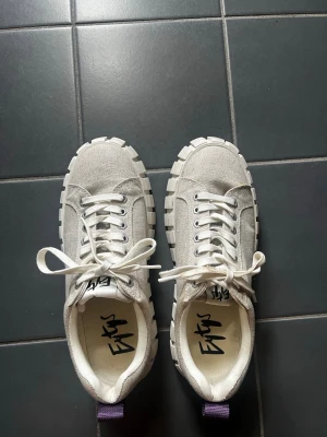 Beiga sneakers från Eytys - Säljer ett par beiga sneakers från Eytys med chunky vit sula och canvasmaterial. Skorna har klassisk snörning, lila hälflik och coolt Eytys-tryck på innersulan. Skorna är små i storleken. 