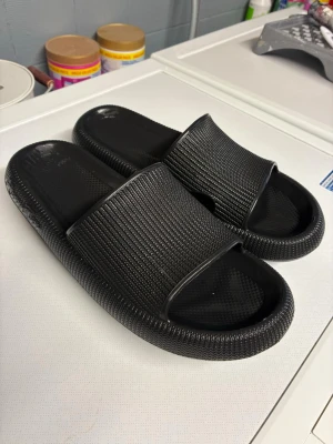 Happy Flops slides i gummi - Säljer ett par svarta Happy Flops med bred rem och öppen tå. Tillverkade i mjukt och flexibelt gummi med räfflad sula för extra grepp. Perfekta för chill dagar hemma eller till stranden. Snygg minimalistisk design som passar till det mesta. Är märkta som 46-47 i storleken men små för mig som har 45 så jag säljer dom som 44. Halva nypriset. 