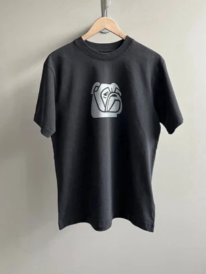 Svart t-shirt med grafiskt tryck - Cool svart t-shirt med ett vitt grafiskt tryck på bröstet som föreställer en stiliserad kamera. T-shirten har rund hals och korta ärmar. Perfekt för dig som gillar minimalistisk design och streetwear-vibe.