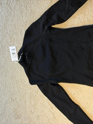 Svart träningsstopp  - Snygg svart träningstopp från Stronger med lång ärm och tight passform. Tillverkad i ett stretchigt material som känns bekvämt mot huden. 