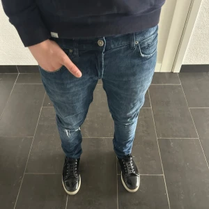 Dondup George - Säljer ett par blå jeans från dondup med modellen George med snygga slitningar på låret och vid bakfickan. Jeansen har klassisk femficksdesign, normal midja och raka ben. Tillverkade i denim med en cool tvättad look och metallknappar. Perfekta för en avslappnad stil.