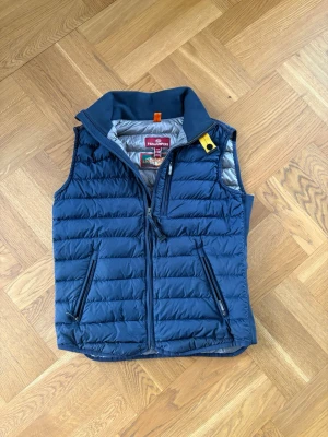 Marinblå ParaJumper Väst - Y-M/XS - Parajumpers väst – marinblå – stl M i kid size så  Snygg och stilren Parajumpers-väst i klassisk marinblå färg. Lätt vadderad modell som är perfekt för vår, höst eller som extra lager under kallare dagar. • Färg: Marinblå • Dragkedja framtill • Två sidofickor med dragkedja • Bröstficka med dragkedja • Parajumpers klassiska gula detalj vid kragen Västen är i fint skick utan hål eller fläckar. Perfekt både till vardag och mer sportig stil. Funkar som XS i herr  Säljes då den inte passar 