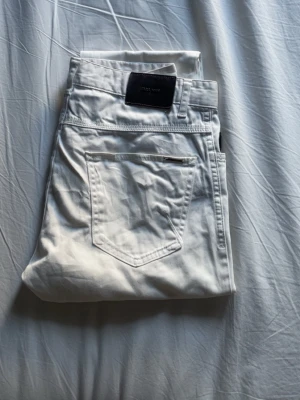 Vita jeans från Zara Man - Snygga vita jeans från Zara Man med klassisk femficksdesign och stilren passform. Jeansen har en mörk läderpatch med logotyp på bakfickan och är tillverkade i ett mjukt bomullsmaterial. Perfekta för dig som vill ha en clean och modern look nu inför sommaren. Använda max två gånger