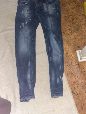 Dsquared2 Byxor Blåa - Säljer ett par blå jeans från Dsquared2 med slitna detaljer och snygg tvätt. Jeansen har klassisk femficksmodell, knappgylf och kontrastsömmar. Perfekta för dig som gillar en avslappnad och trendig stil.