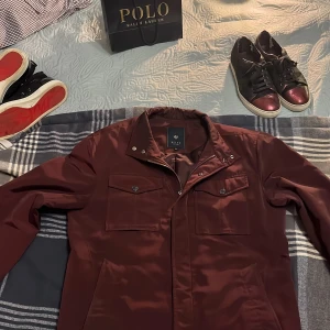 Field jacka  - Säljer en snygg vinröd jacka från Riley i storlek 52. Jackan har en stilren design med knappar och dragkedja framtill. Perfekt för höst och vår med sina långa ärmar och praktiska fickor. Passar både till vardags och lite finare tillfällen. Har du frågor så är det bara att skriva Nypris:1299 