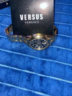 Versus Versace guld herrklocka - Snygg guldig klocka från Versus Versace med svart urtavla och metallarmband. Klockan har flera små urtavlor och detaljer i guld, vilket ger en lyxig och modern look. Perfekt accessoar för dig som vill sticka ut. Den är från år 2021! Batteri måste bytas, vattentät.                                        Tar emot byten 