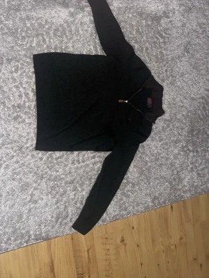 Mörkgrön stickad tröja Morris - Mörkgrön stickad tröja från Morris i 100% merinoull. Tröjan har lång ärm och en half zip-dragkedja framtill med en snygg liten läderdetalj på dragkedjan. Perfekt för dig som gillar klassisk och stilren design.