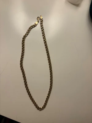 Bismarck, safira - Snyggt halsband med klassisk kedjedesign i guldtonad metall. Halsbandet har en enkel och stilren look med robusta länkar och ett smidigt spänne. Perfekt för att lyfta din outfit med en trendig touch.