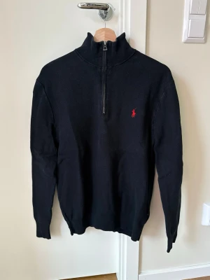 Svart halvzip Ralph Lauren - Klassisk svart stickad tröja från Ralph Lauren med halv dragkedja och hög krage. Passar S/M