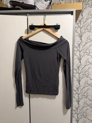 Mörkgrå offshoulder topp - Trendig mörkgrå offshoulder topp med lång ärm. Snygg och enkel design som passar perfekt till jeans eller kjol. Tillverkad i mjukt material för en bekväm känsla och tight passform.