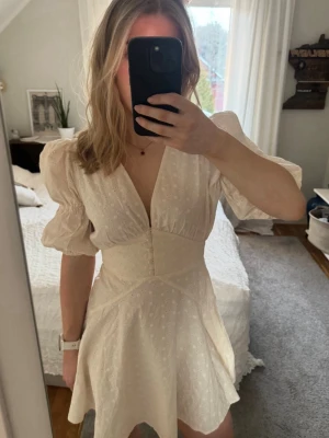 Cremevit kortklänning med puffärm - Söt cremevit kort klänning från Adoore med puffärmar och v-ringning. Klänningen har markerad midja och lätt utställd kjol, prislapp kvar💗