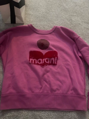 Rosa hoodie från Isabel marant - Cool rosa hoodie från Isabel marant med tryckt logga i rött och vitt framtill. Mjuk insida och ribbade muddar vid ärmslut och nederkant. Perfekt för en avslappnad och trendig look.