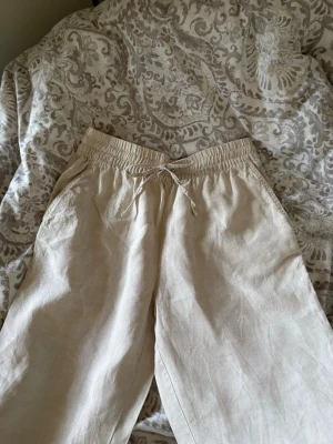 Beige linnebyxor - Säljer ett par beige linnebyxor med avslappnad passform och elastisk midja med dragsko. Byxorna har sidofickor och är tillverkade i ett lätt och luftigt linnematerial, perfekt för en chill och stilren look.